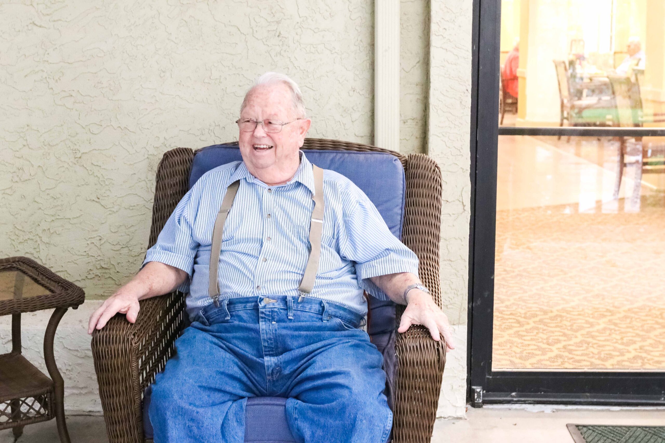 Smiling resident sitting in wicker chair on the patio at Sedgwick Plaza, a top choice for senior living.