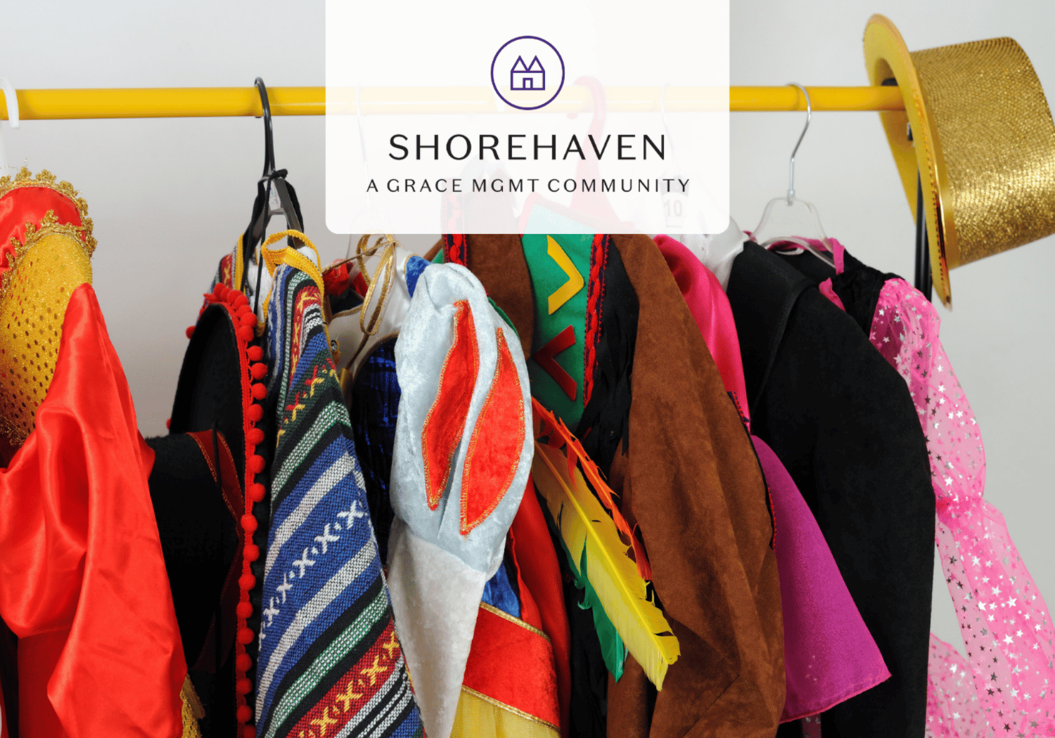 Rack of colorful costumes on hangers with a white banner featuring the Shorehaven logo and 'A Grace Mgmt Community' across the top.